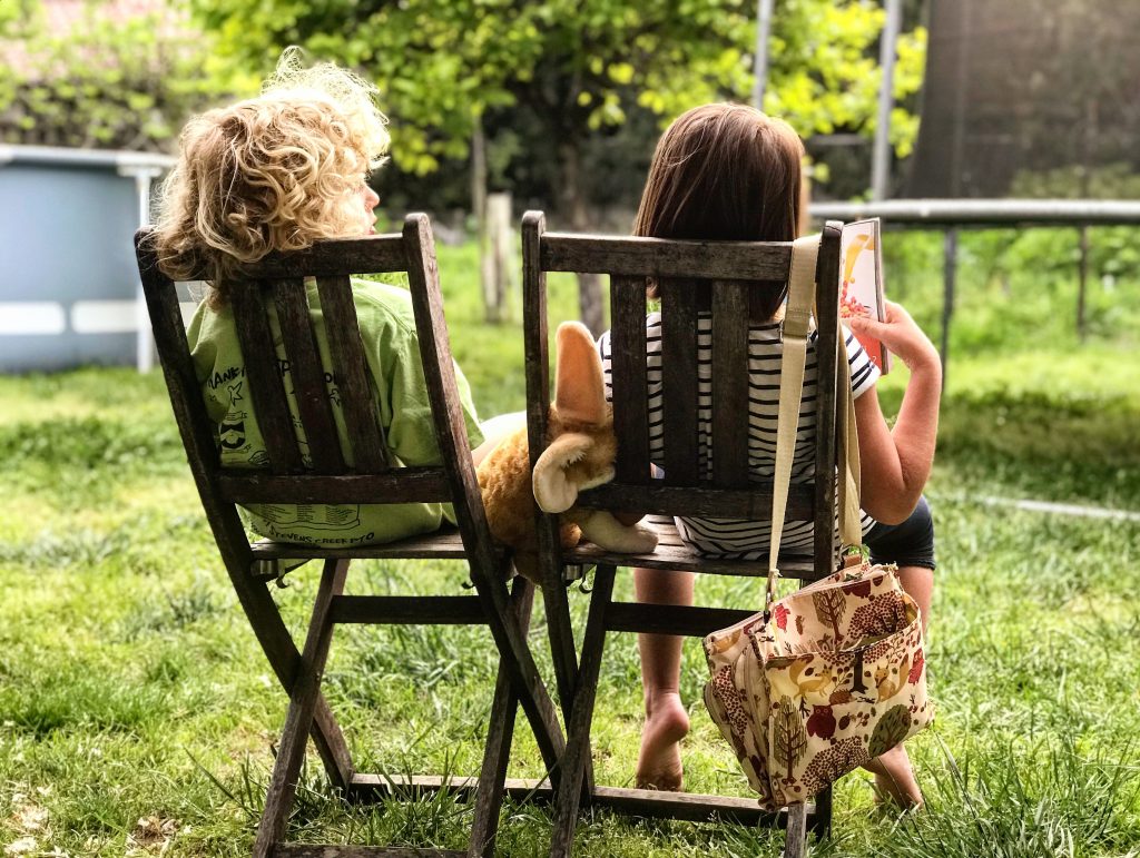 Two children sit on patio chairs in the garden