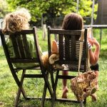 Two children sit on patio chairs in the garden
