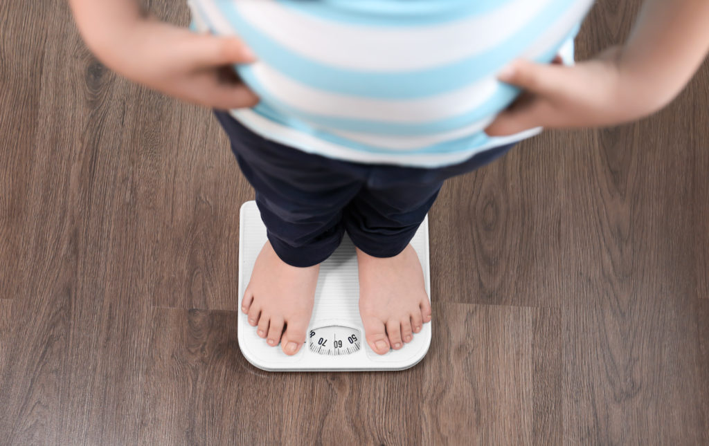 MOTHERS! IS WORKING FOR A LIVING MAKING YOUR KIDS FAT? Overweight boy standing on floor scales indoors: