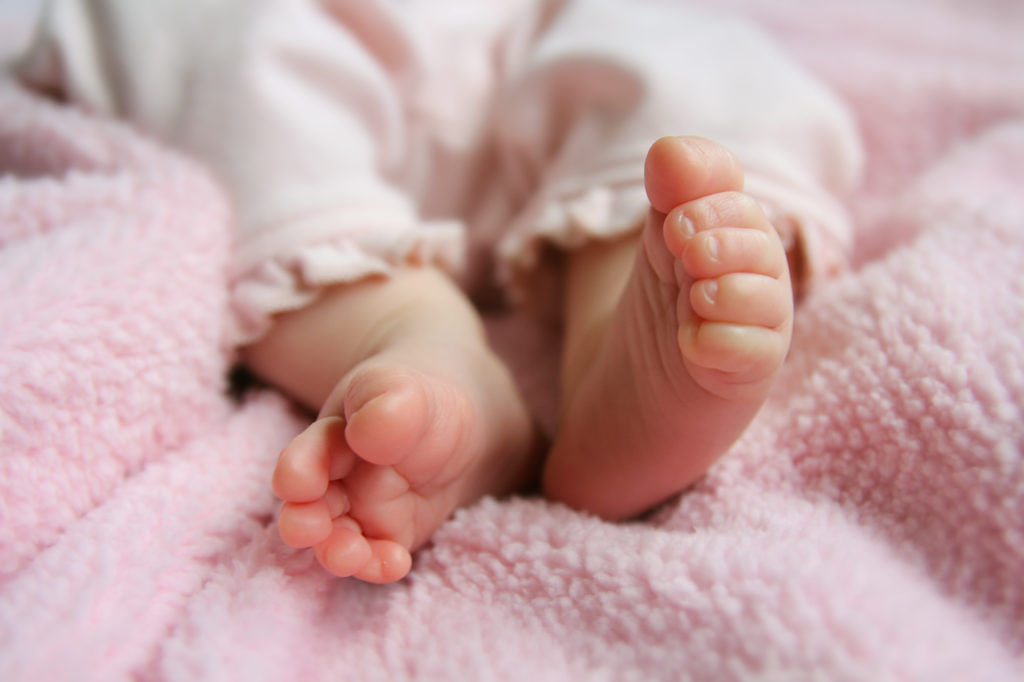 A close up portrait of the bottoms of a newborn baby girl's feet on pink blankets.